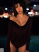 A woman in a black bodysuit standing by a pool at night.