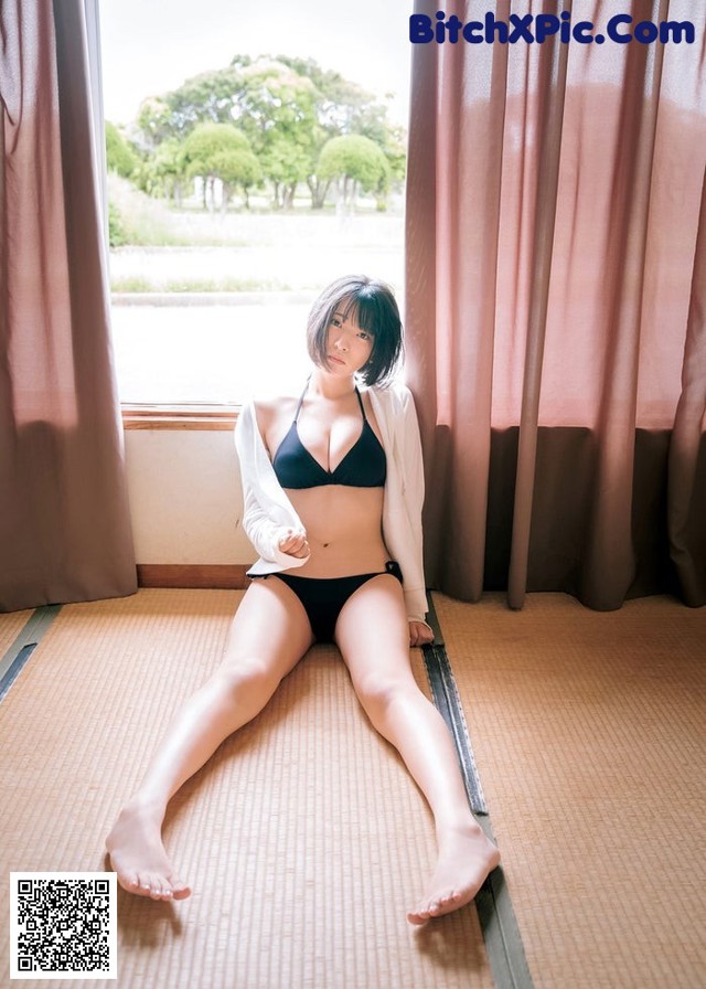 A woman in a black bikini sitting on a tatami mat.