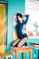 A woman in a blue bodysuit sitting on a stool.