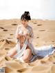 A woman in a white dress sitting on a sand dune.