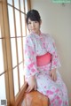 A woman in a pink and white kimono sitting on a window sill.