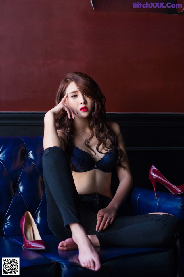 A woman sitting on a blue couch wearing red high heels.