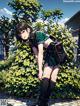 A girl in a school uniform with a backpack standing in front of a bush.