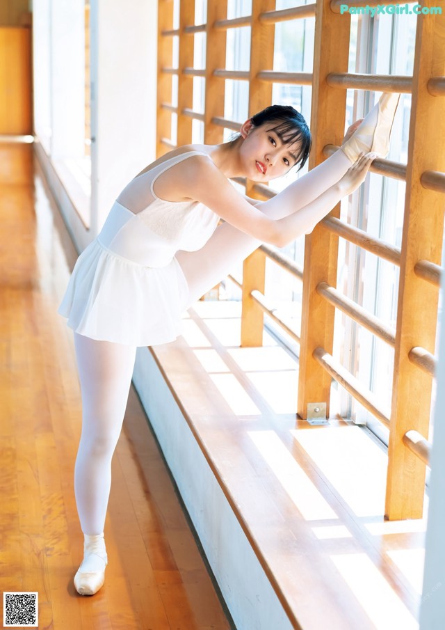 A woman in a white leotard and pointe shoes leaning against a window.
