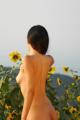 A naked woman standing in a field of sunflowers.