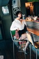 A woman sitting at a bar in a white shirt and black skirt.